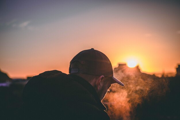 Flacher, fokussierter Schuss des Rückens eines Mannes mit Mütze während der goldenen Stunde des Sonnenuntergangs.