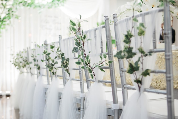 Flacher fokussierter Schuss von schönen silbernen Stühlen, die für eine Hochzeit nahe einem Hochzeitstisch verziert werden