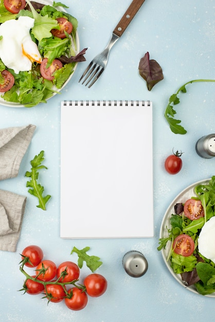Flacher Salat mit Spiegelei und Tomaten mit leerem Notizbuch