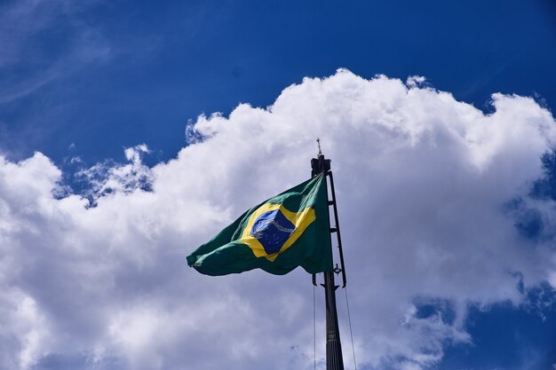 Flacher Winkelschuss der Flagge von Brasilien unter den schönen Wolken im blauen Himmel