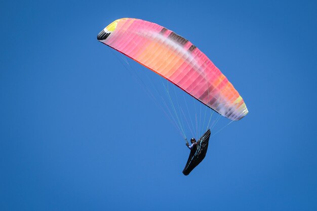 Flacher Winkelschuss einer Person, die an einem sonnigen Tag unter dem hellen Himmel Paragliding ist
