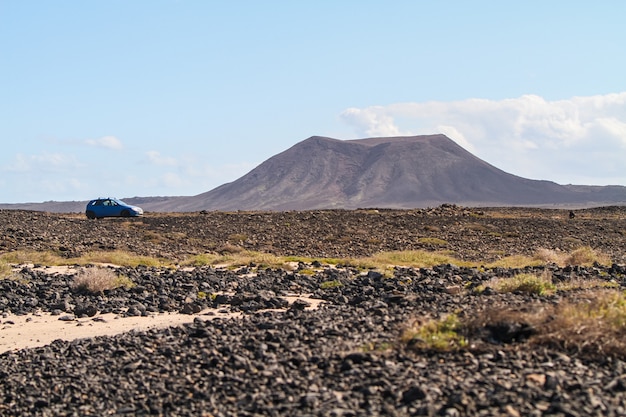 Flacher Winkelschuss eines blauen Autos, das neben einem Hügel in Fuerteventura, Kanarische Inseln geparkt wird