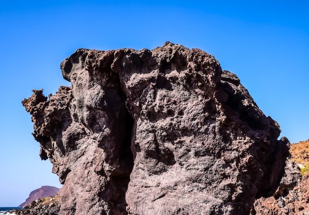 Flacher Winkelschuss eines großen Felsens an einem Strand mit einem klaren blauen Himmel