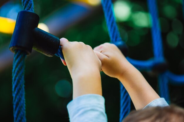 Flacher Winkelschuss eines Kindes, das an einem blauen Kletterspielzeug auf dem Spielplatz eines Parks festhält