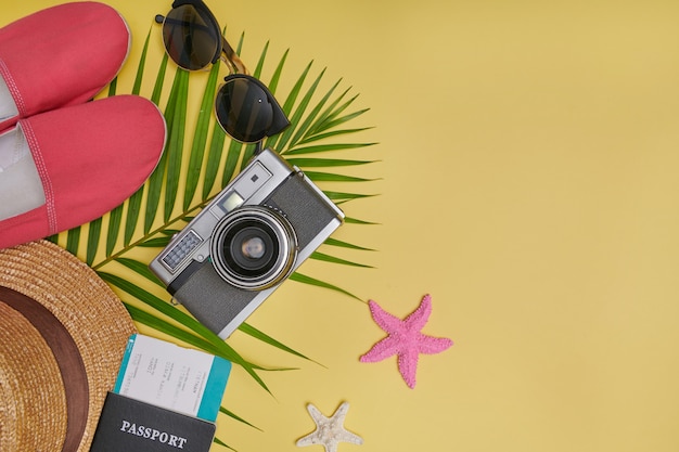 Flaches Reiseaccessoire auf gelbem Hintergrund mit Palmblatt, Kamera, Schuh, Hut, Pässen und Sonnenbrille. Draufsicht Reise- oder Urlaubskonzept. Sommergelber Hintergrund.