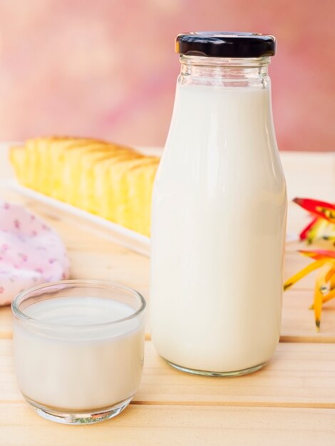 Flasche mit Glas Milch- und Butterkuchen auf weißem Holztisch.