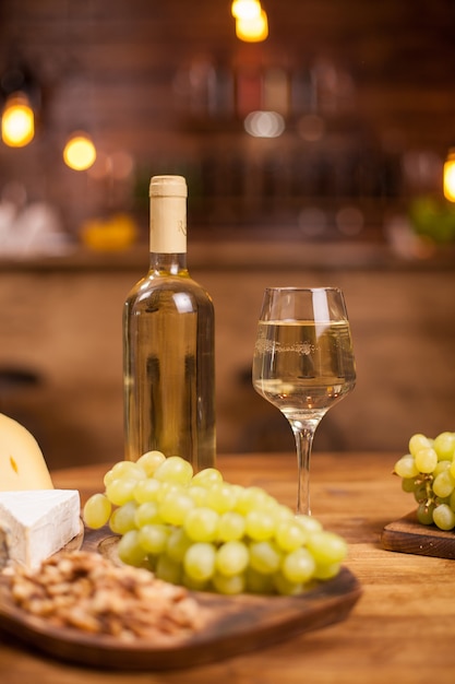 Flasche Weißwein ein Glas voll davon neben verschiedenen Käsesorten. Frische Trauben. Leckere Walnüsse.