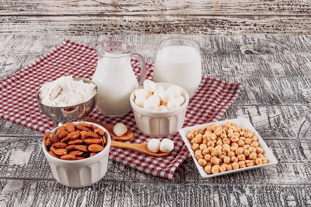 Flaschen Milch mit Käse und Holzlöffel, Mandeln, Haselnuss-Hochwinkelansicht auf einem grauen hölzernen Hintergrund