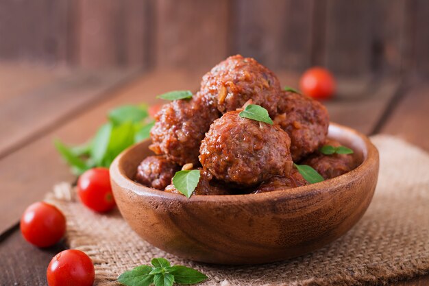 Fleischbällchen in süß-saurer Tomatensauce und Basilikum in einer Holzschale