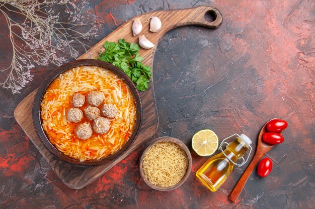 Fleischbällchensuppe mit Nudeln an Bord ungekochte Nudeln Zitronengrün Tomaten Ölflasche auf dunklem Hintergrund