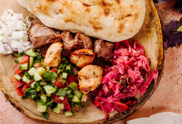 Fleischgrill mit Gemüsesalat und mariniertem Kohl auf einem Stück Holz.