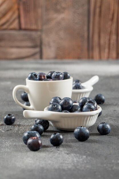 Fleischige Blaubeeren in der Seitenansicht der Tasse und der Schöpflöffel auf grauer Oberfläche