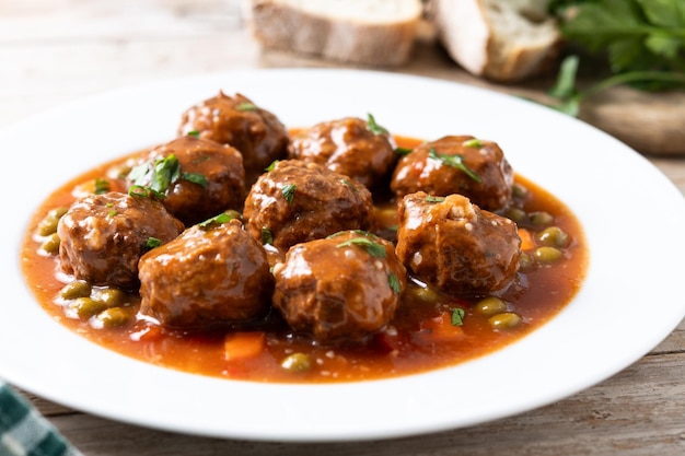 Fleischkugeln, grüne Erbsen und Karotten mit Tomatensauce auf einem Holztisch