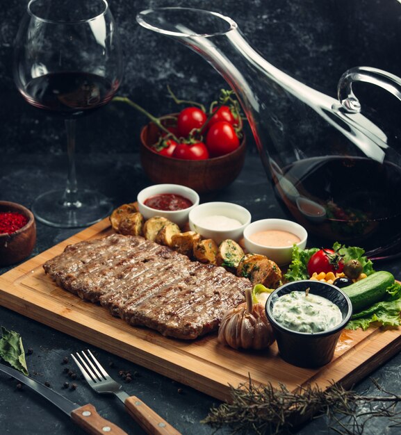 Fleischsteak mit Dip-Sauce und Dressings auf einem Holzbrett.