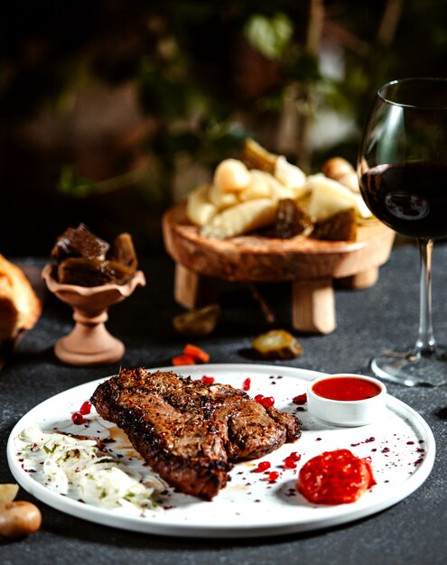 Fleischsteak von vorne auf einem Teller mit Zwiebelketchup und einem Glas Rotwein