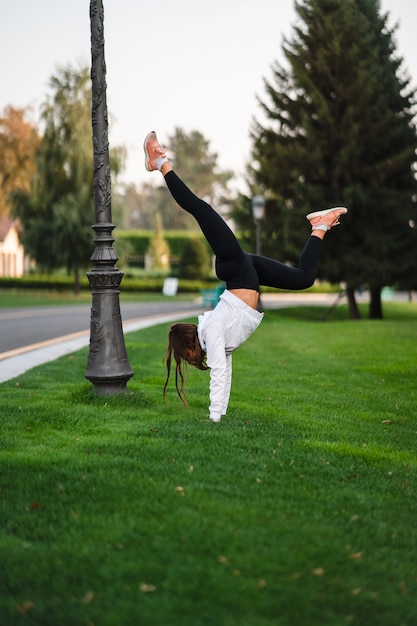 Flexibler Turner. Attraktive dünne Frau, die einen Backbend macht, während sie einen Salto zeigt. Draußen