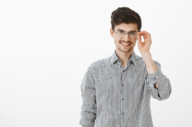 flirty nerdy Kerl in runden Gläsern mit Bart und Schnurrbart, hält Brillenrand und lächelt breit, fühlt sich sicher und entspannt, nachdem er dem attraktiven Mädchen in der Bar die Abhollinie gesagt hat