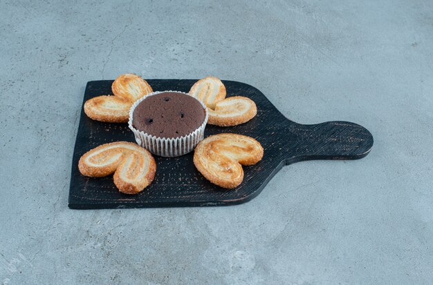 Flockige Kekse und ein Cupcake auf einer schwarzen Tafel auf Marmorhintergrund. Hochwertiges Foto