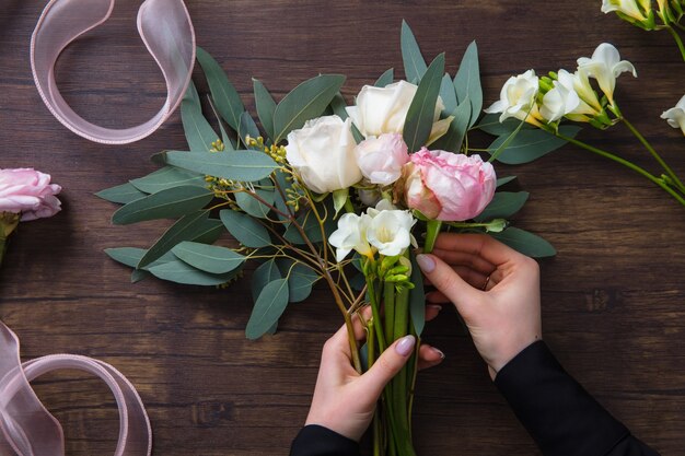 Floristische Frau, die modernen Blumenstrauß der Mode verschiedener Blumen auf hölzernem Hintergrund macht