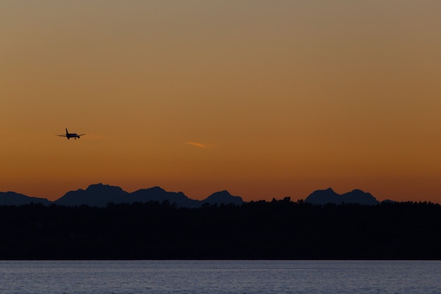 Flugzeug fliegt über Hügel und Meer bei Sonnenuntergang