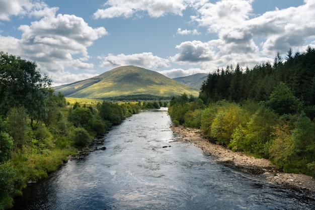 Fluss, der durch die Bäume und Berge in Schottland fließt