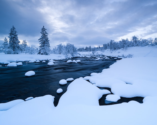 Fluss mit Schnee und ein Wald in der Nähe mit Schnee im Winter in Schweden bedeckt
