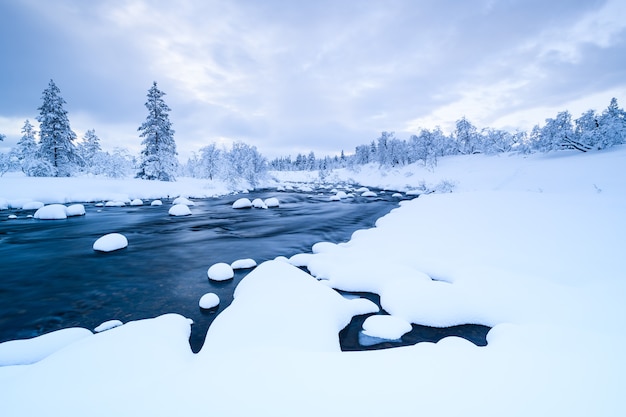 Fluss mit Schnee und ein Wald in der Nähe mit Schnee im Winter in Schweden bedeckt