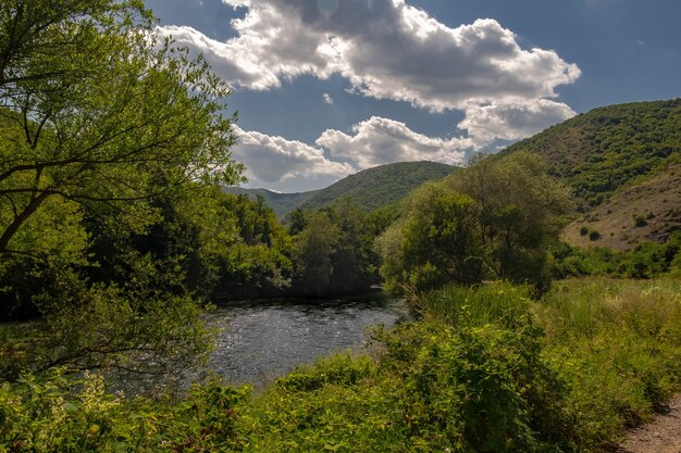 Fluss umgeben von grünen Hügeln unter dem Sonnenlicht und einem blauen Himmel