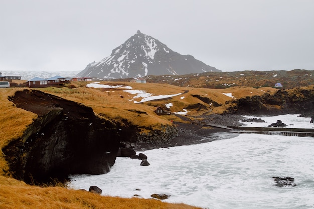 Fluss umgeben von Hügeln mit viel Grün und Schnee in einem Dorf in Island