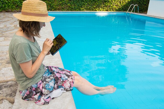 Fokussierte Frau im Strohhut, die am Pool sitzt