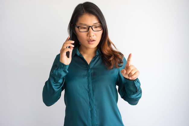 Fokussierte junge Asiatin, die oben am Telefon mit dem Finger spricht.