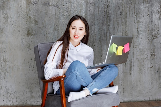 Fokussierte junge Frau, die auf einem Sessel sitzt und am Laptop arbeitet. Foto in hoher Qualität