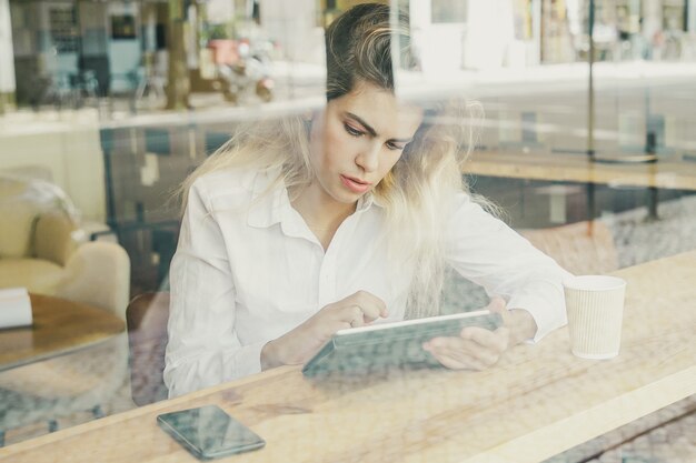 Fokussierte weibliche Fachkraft, die am Schreibtisch im gemeinsamen Arbeitsraum oder im Café sitzt, unter Verwendung des Tablets