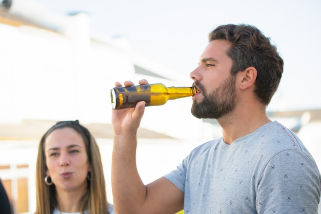 Fokussierter bärtiger Kerl, der Bier mit Freunden genießt