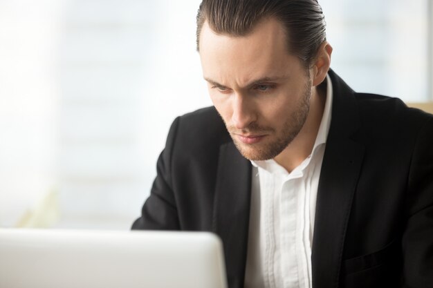 Fokussierter Geschäftsmann, der auf Laptopbildschirm schaut