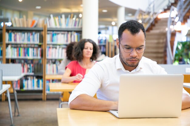 Fokussierter männlicher erwachsener Student, der an Computer im Klassenzimmer arbeitet