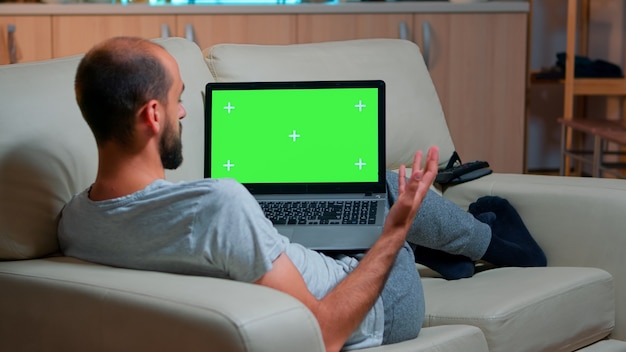 Fokussierter mann, der laptop-computer mit nachgebildetem greenscreen-chroma-key-display sucht