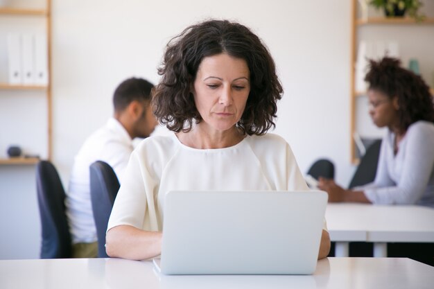 Fokussierter weiblicher Angestellter, der an Laptop im Büro arbeitet