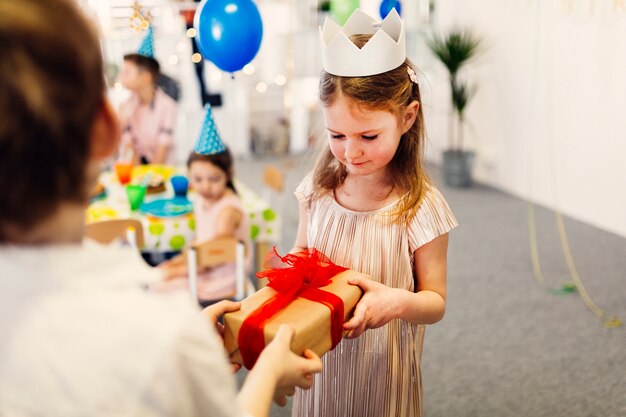 Fokussiertes Mädchen in der weißen Krone, die Geschenk nimmt