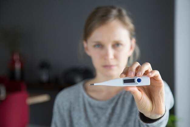 Fokussiertes Nahaufnahmebild des Thermometers gehalten von der kranken jungen Frau