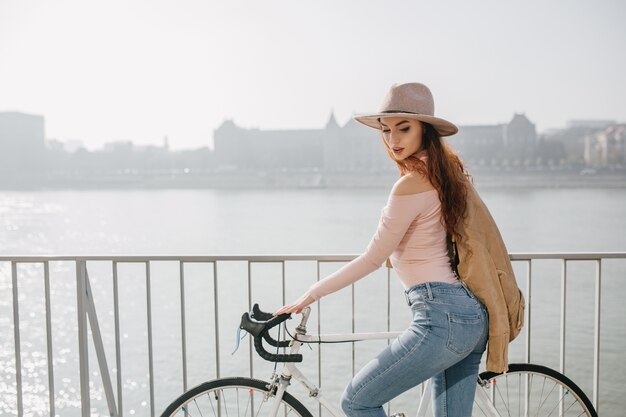 Formschöne rothaarige Frau, die mit dem Fahrrad die Brücke hinunter fährt