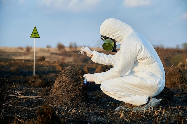 Forscher im Schutzanzug, der auf einem verbrannten Feld arbeitet und Pflanzenproben nimmt