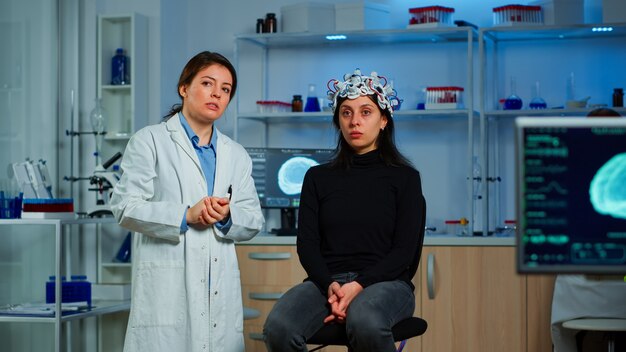 Forscher und Patient mit EEG-Headset mit Blick auf virtuelles Display mit Touchscreen, virtuelle Realität mit medizinischer Innovation im neurologischen Forschungslabor. Wissenschaftler, die mit Gesundheitssimulator arbeiten