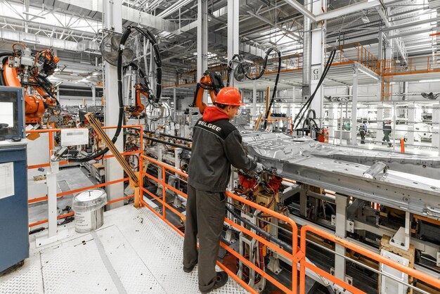 Foto der Automobilproduktionslinie Schweißkarosserie Modernes Automontagewerk Autoindustrie Männlicher Arbeiter in einem orangefarbenen Schutzhelm