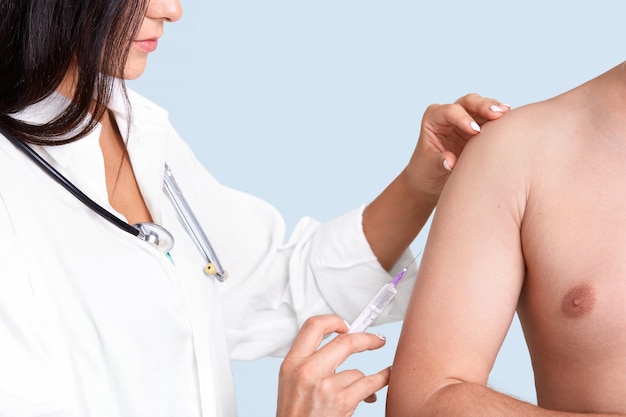 Foto der brünetten weiblichen Krankenschwester im weißen Kleid mit Phonendoskop, macht Impfung im Arm zum Patienten