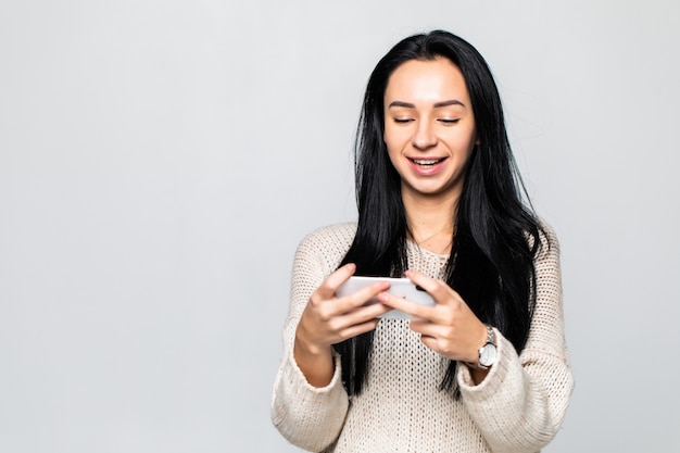 Foto der emotionalen glücklichen fröhlichen jungen Frau, die Spiele durch Handy spielt, das lokal über weißer Wandwand aufwirft