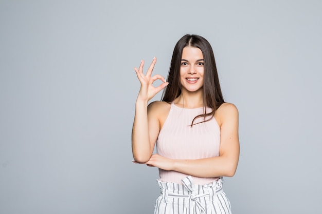 Foto der hübschen jungen lächelnden frau, die lokal über weißer wand steht.