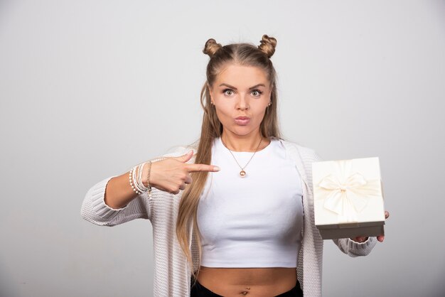 Foto der jungen Frau, die auf eine Geschenkbox zeigt.