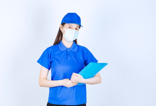 Foto der jungen Frau in medizinischer Maske, die Ordner steht und hält.