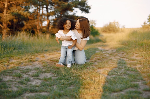 Foto der kaukasischen Mutter und ihrer afroamerikanischen Tochter, die sich draußen zusammen umarmen. Mädchen hat schwarzes lockiges Haar